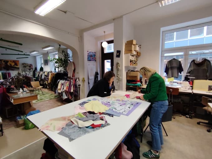 V enem delu velikega prostora je delavnica, ustvarjalnica novih oblačil iz (starega) blaga, v drugem prodajni del.
