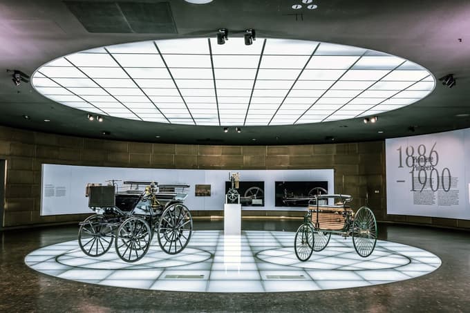 Benz Patent-Motorwagen (desno) in Daimler Motorkutsche (levo) na razstavnem prostoru, ki zajema obdobje od leta 1886 do 1900. V središču je Daimlerjeva "stoječa ura" – prvi majhen, hitrovrteči se motor z notranjim zgorevanjem.