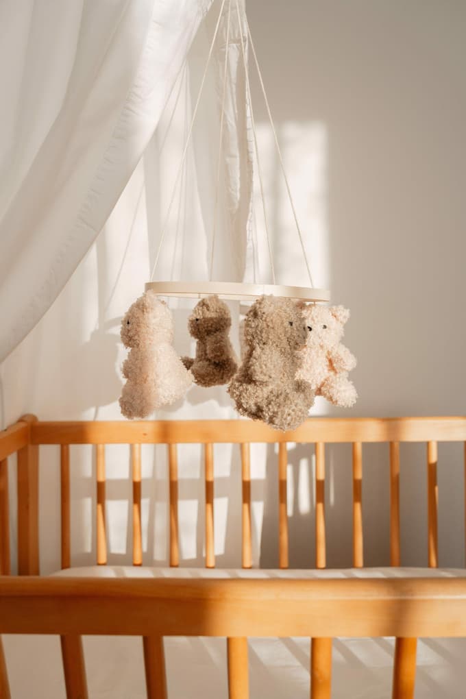 Minimalistično opremljena otroška soba, ki ji mehkobo dodajajo les in igrače umirjene barvne palete.