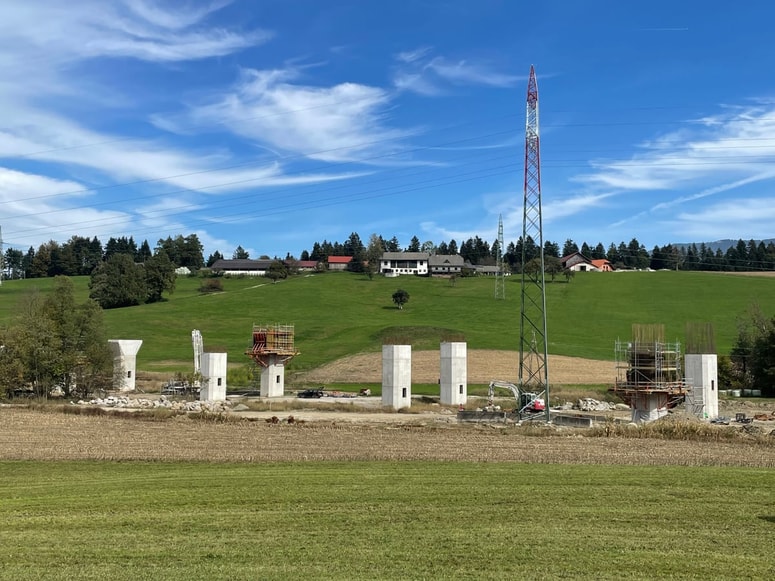 Gradbišče pri Podgorju s kmetijo Krevh v ozadju ter s stebri hitre ceste in povišanim elektrovodom v ospredju 