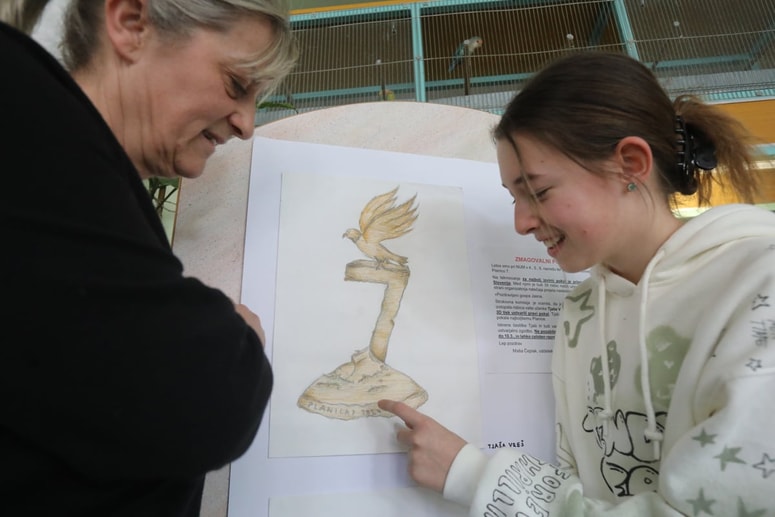 Jasna Antolinc in Tjaša Vreš ob originalni zmagovalni risbi, razstavljeni v avli OŠ Rada Robiča Limbuš 