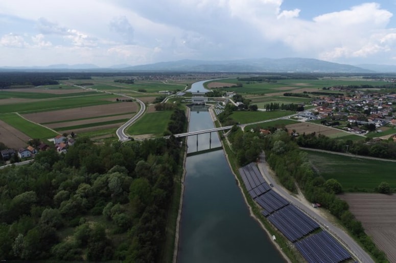 Pogled na zgrajeno sončno elektrarno na brežini odvodnega kanala; v ozadju hidroelektrarna Zlatoličje – največja slovenska hidroelektrarna. 