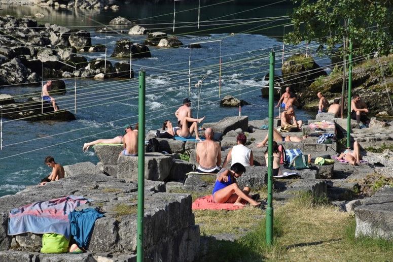Na obali pri kajakaškem centru se večina sonči. Nekateri se osvežijo v mirni vodi, nekateri pa tudi tvegajo s plavanjem čez brzice na nasprotni breg Soče. 