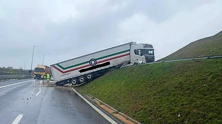 Glavna fotografija članka:Tovornjak s priklopnikom zapeljal z vozišča na brežino in obtičal z dvignjenimi kolesi