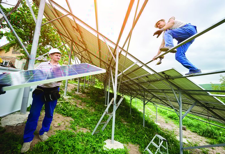 Installing of solar photo voltaic panel system. Three technicians lifting heavy solar module on high platform. Investment in alternative energy, money saving and professional construction concept.