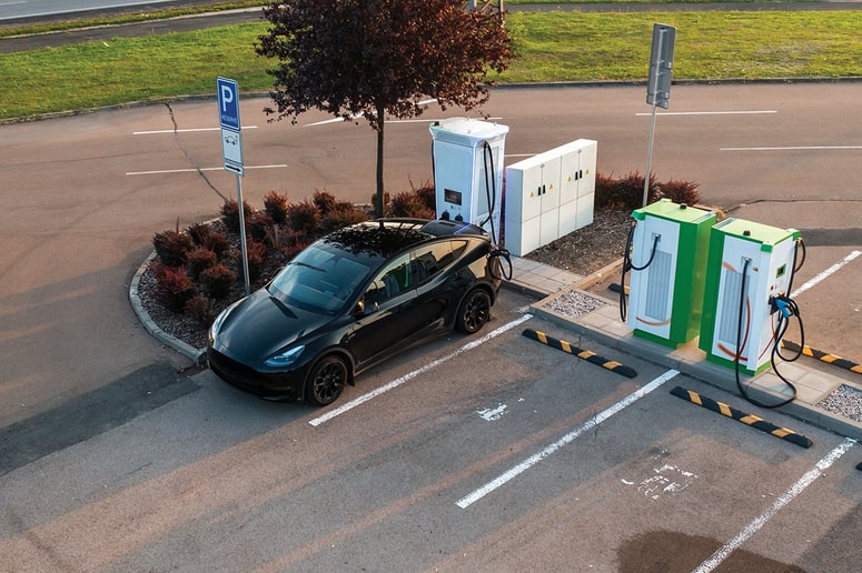 Black electric vehicle is receiving power at a public charging point, top view. 