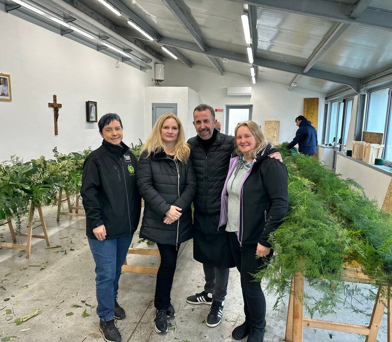 Trojica okraševalcev v vrtnarji, kjer so v četrtek začeli pripravljati podlage za cvetlično okrasje, s Tino Kokalj iz slovenskega veleposlaništva pri Svetem sedežu. 